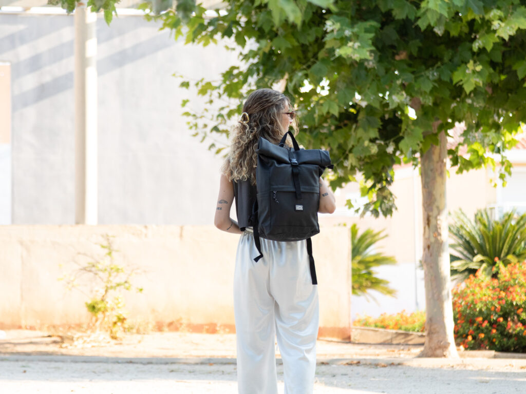 Chica de espaldas paseando con una mochila ligera para turismo negra de ALE-HOP y ropa veraniega.