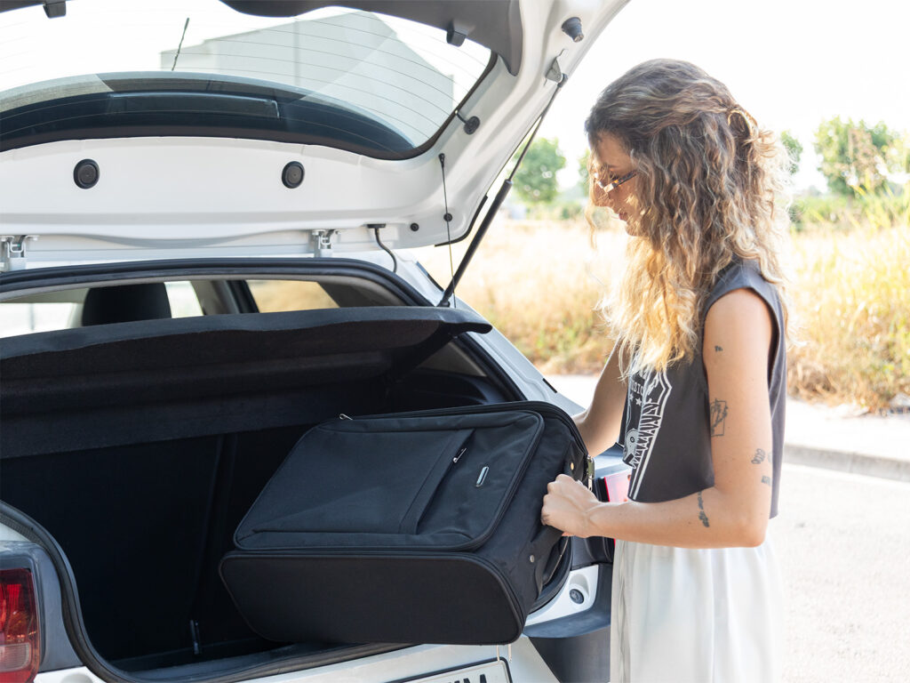 Chica guardando una maleta de cabina negra en el maletero del coche para empezar su viaje.