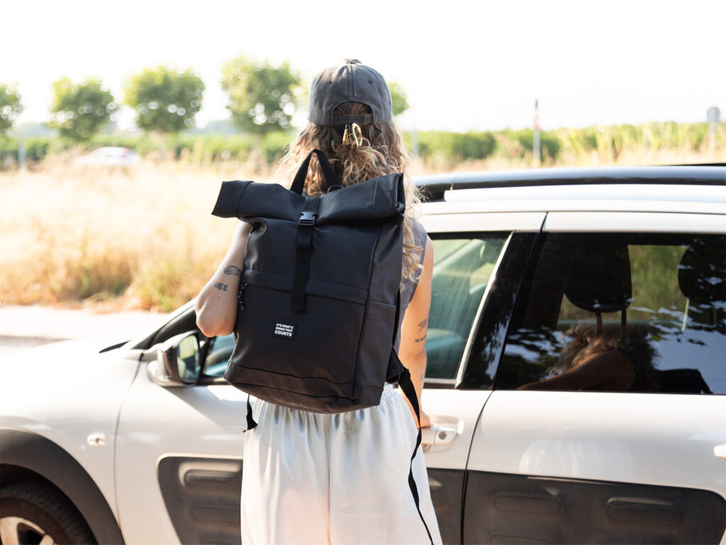 Chica con gorra gris abriendo la puerta del coche con una mochila viaje de ALE-HOP de estilo roll top.