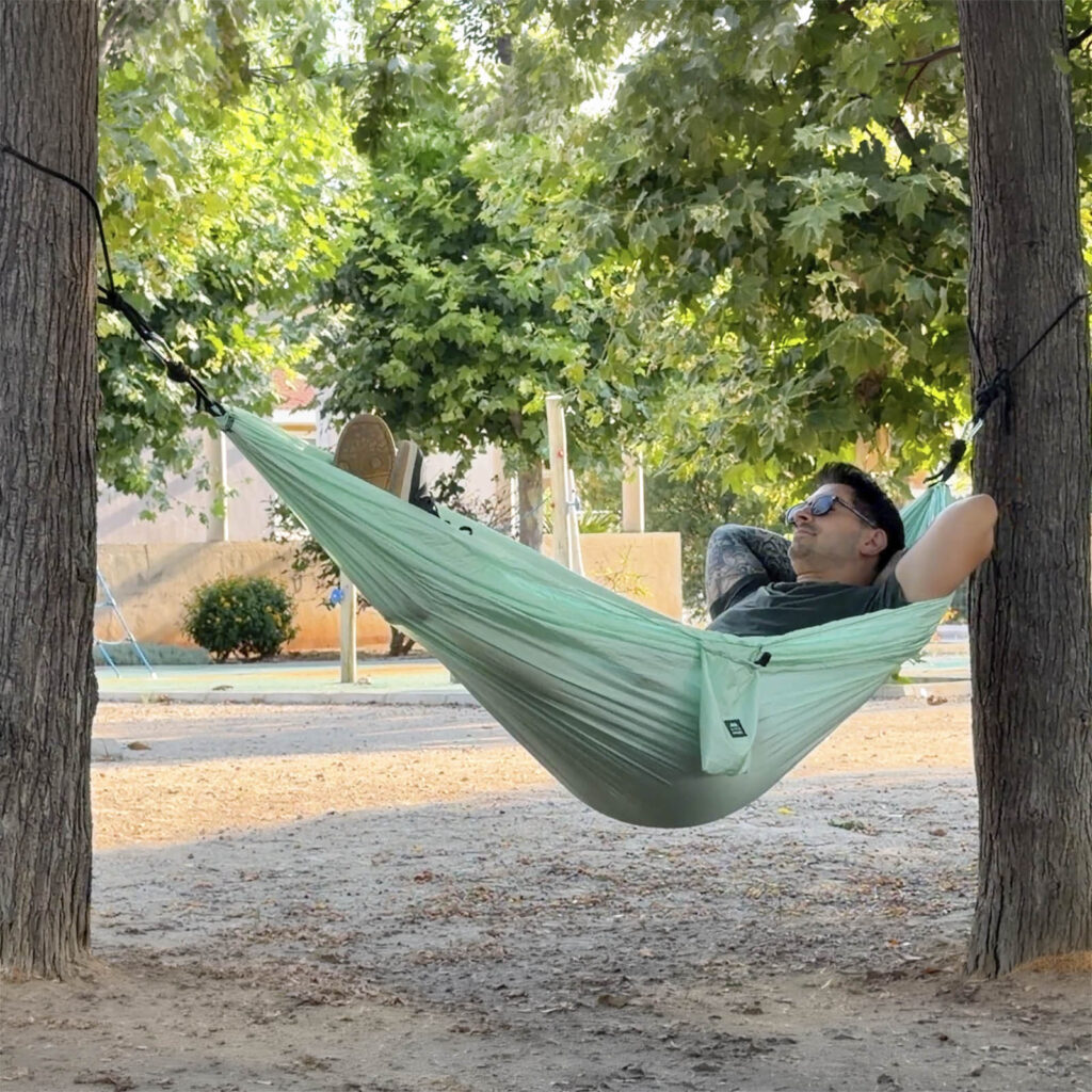 Hombre con gafas de sol relajado en una hamaca ligera para acampar entre árboles de ALE-HOP.