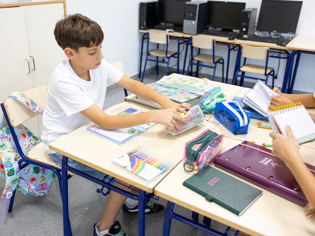 Alumno en clase organizando su estuche escolar transparente con bolífragos divertidos y marcadores.