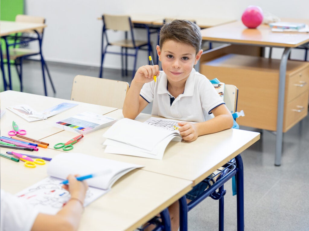 Alumno en el aula con tijeras infantiles, libretas bonitas y rotuladores de colores.