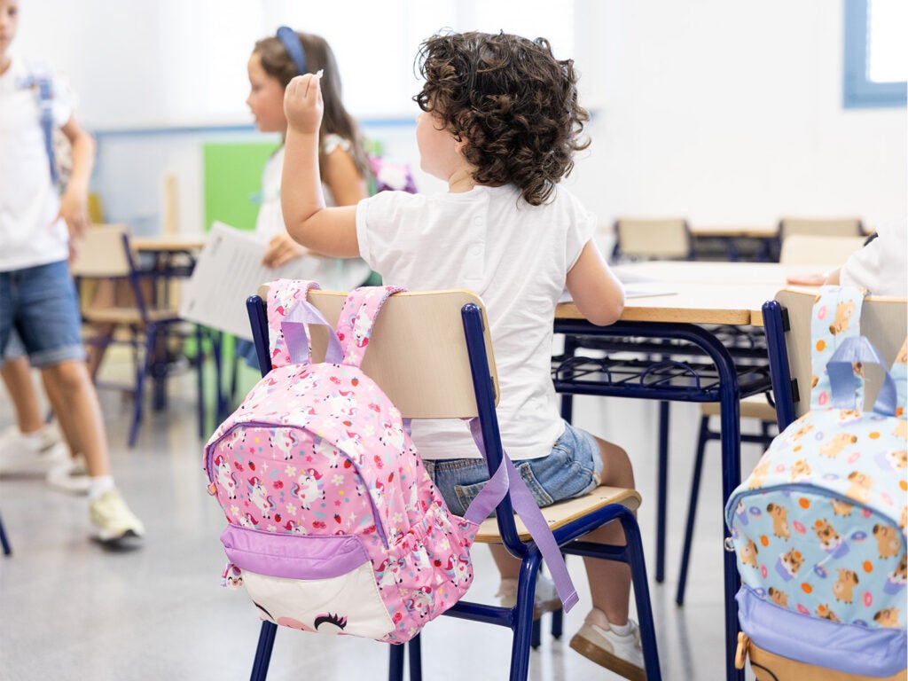 Niña en clase con mochila escolar infantil de unicornio colgada en la silla.