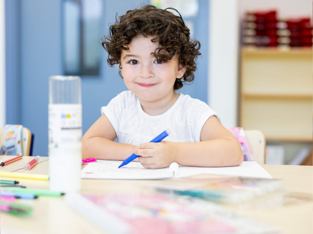 Niña sonriente dibuja en su cuaderno escolar con rotuladores de colores.