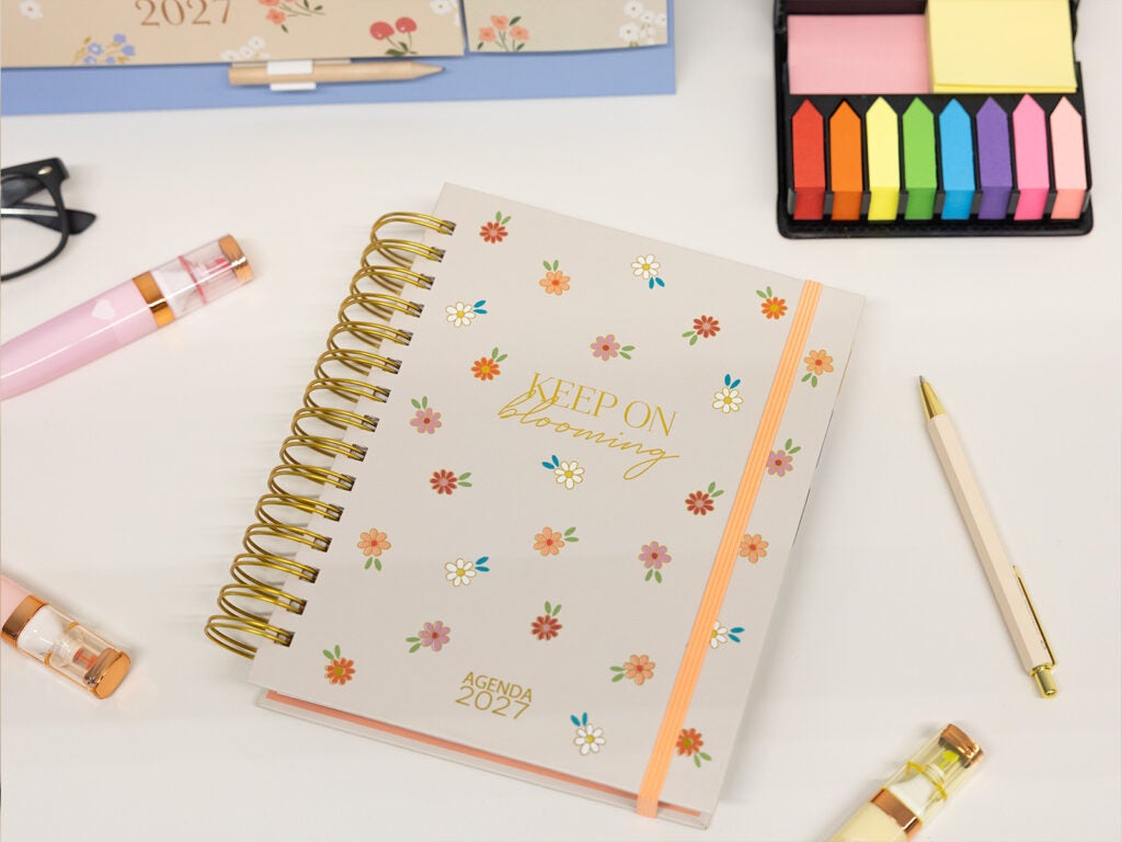 Agenda anual bonita 2027 de espiral dourada com flores na mesa