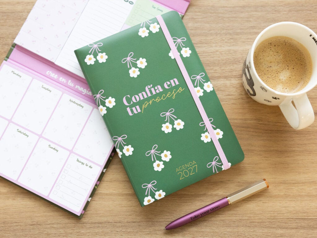 Agenda anual 2027 de capa dura verde ao lado de um planeador e café